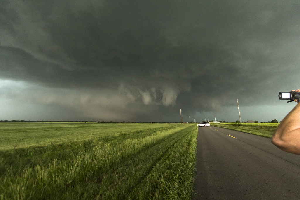 Tornadoes form far in the distance on the plains, a man holds a camera to film.
