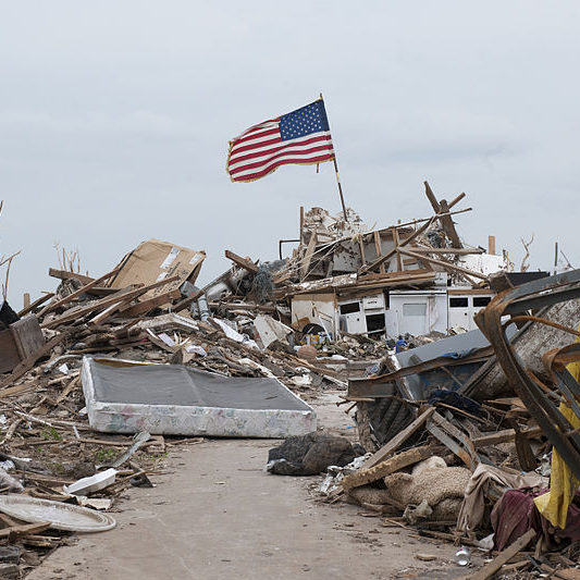 An american flag stands above a destroyed homestead, storm shelters save lives.