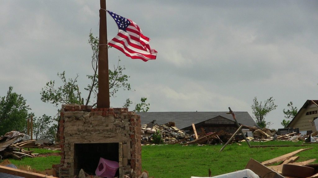 Oklahoma home destroyed by tornado with american flag waving in the wind.