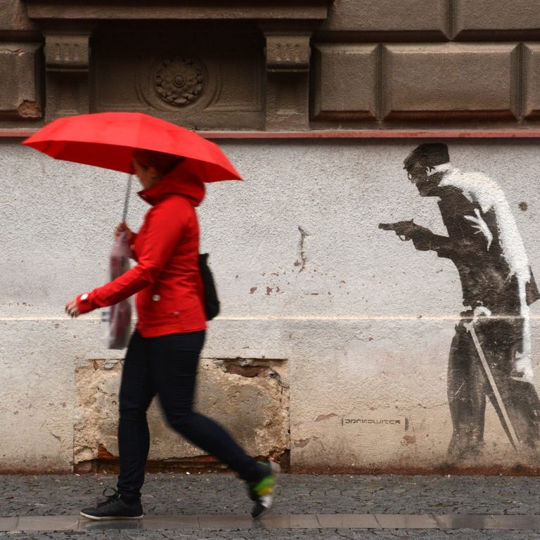 A woman walks by a painting that points a gun at her back.